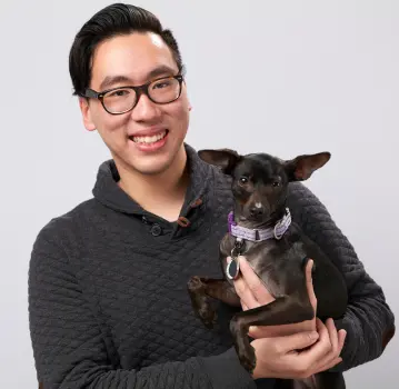 Person with glasses holding a small dog.